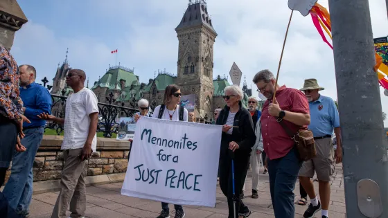 People walk past Parliament hill holding a sign that reads "Mennonites for a just peace"