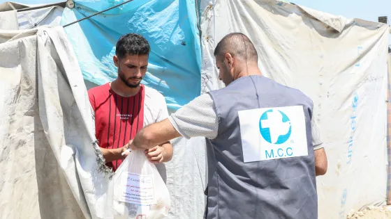 A man wearing an MCC vest hands a bag of food to a man.