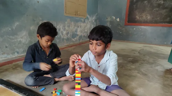Two boys from India play with blocks in a bare room. 