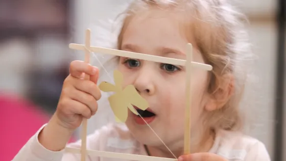 child blows bubble through square made of popsicle sticks
