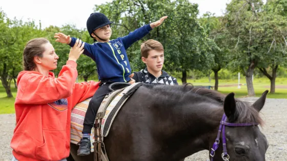 The 6-year-old child* on the horse is assisted during therapy for children who are displaced and affected by war.  MCC, with partner Association of Mennonite Brethren Churches of Ukraine (AMBCU),