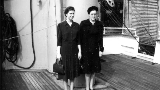 Black and white photo of two women standing together on the deck of a ship. They are smiling.